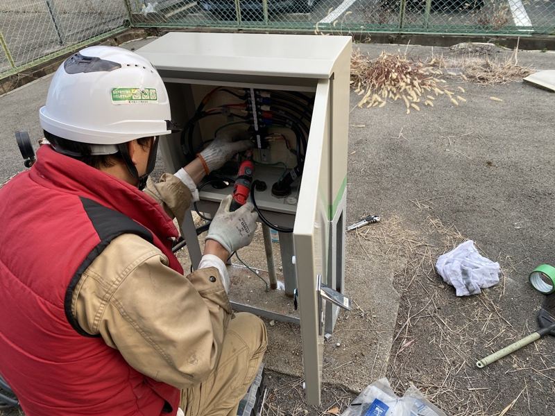 屋外の制御盤で結線作業をする作業員